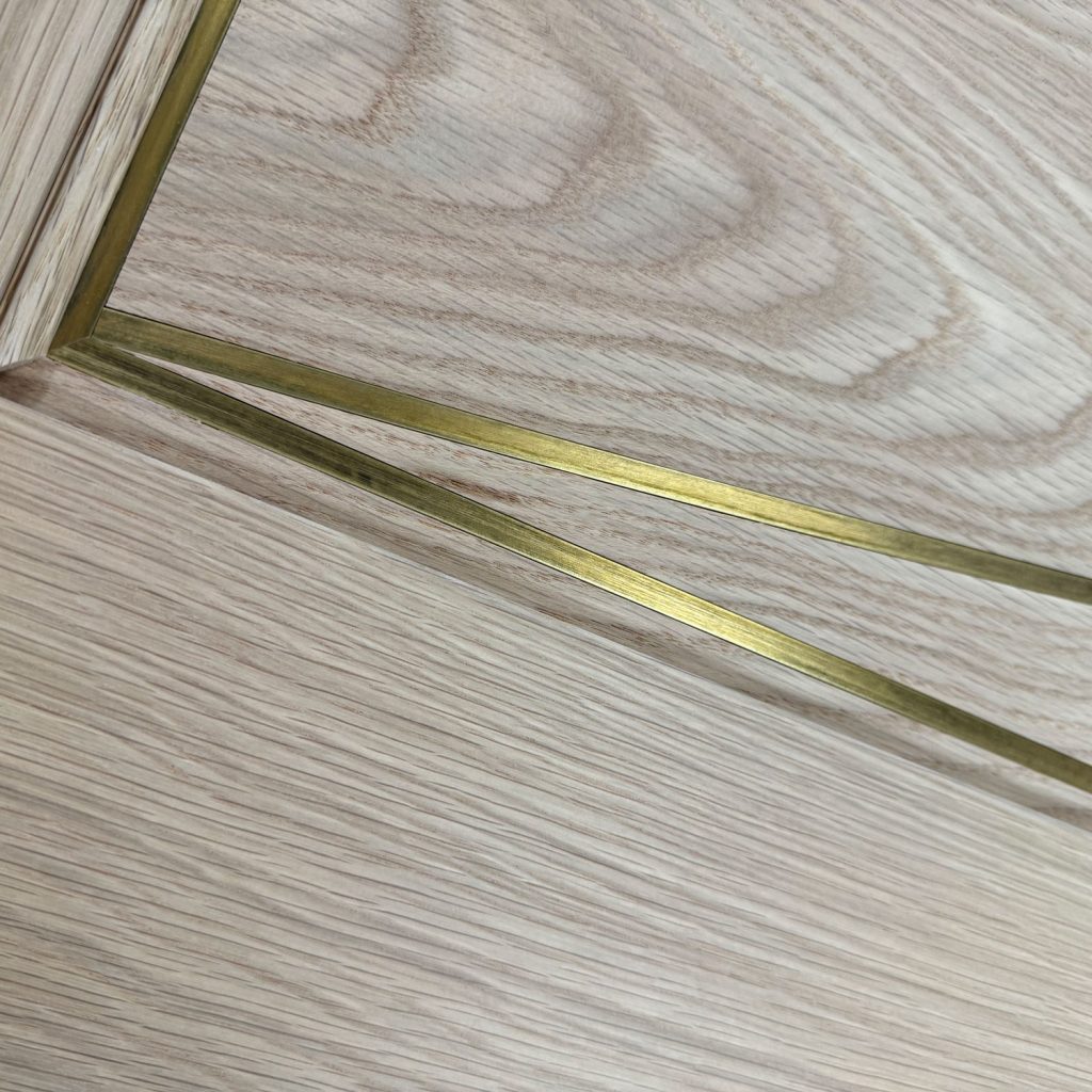 Close-up of white oak wood door with precision-set brass inlay, crafted by Rockwood Door & Millwork in Millersburg, Ohio for a luxury interior application.